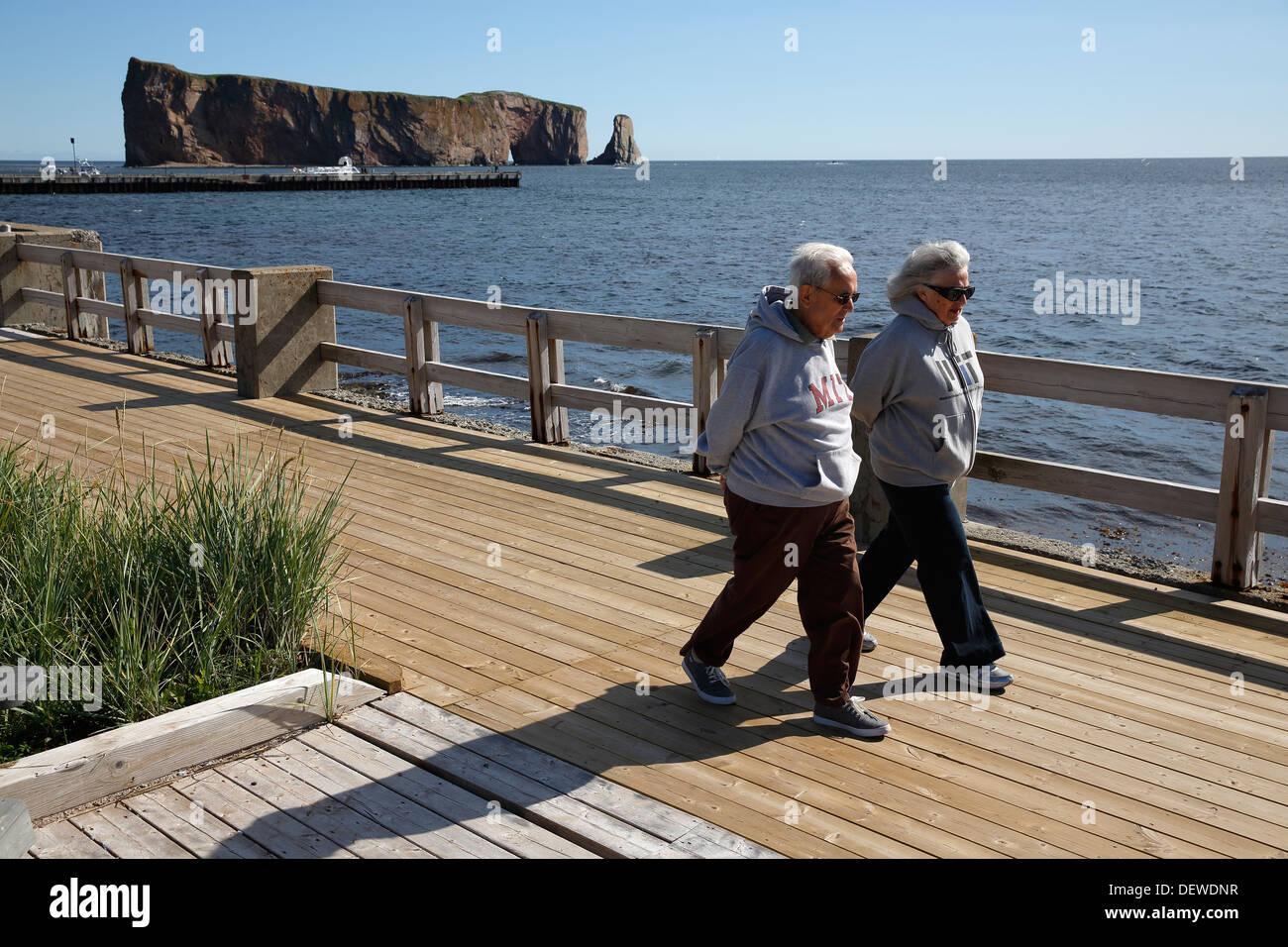 A couple walking on the boardwalk with Percé Rock in the background,  Percé Québec Canada Stock Photo