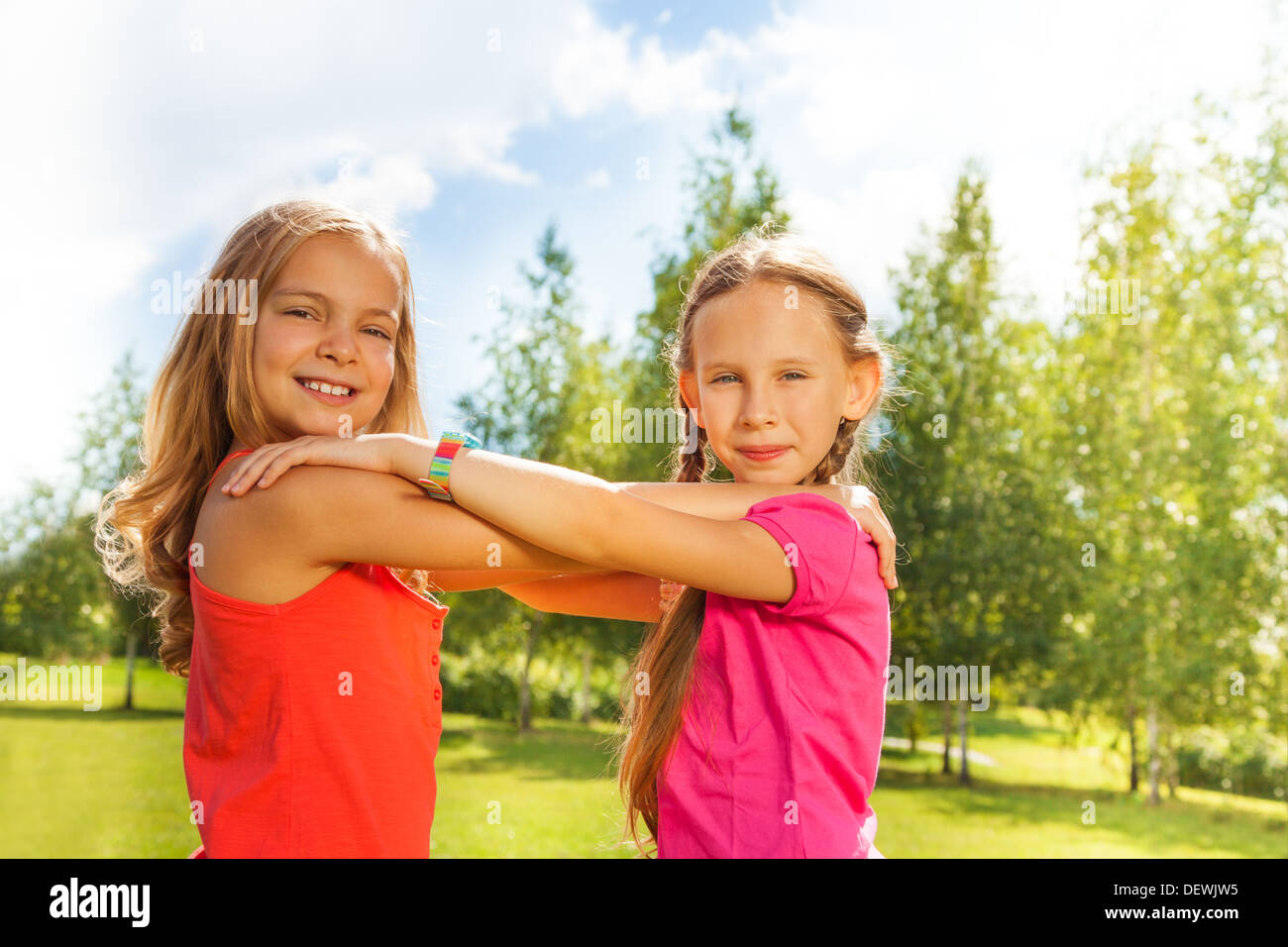 Portrait of two girls bright orange shirts holding hands together and dancing in the park on sunny day Stock Photo