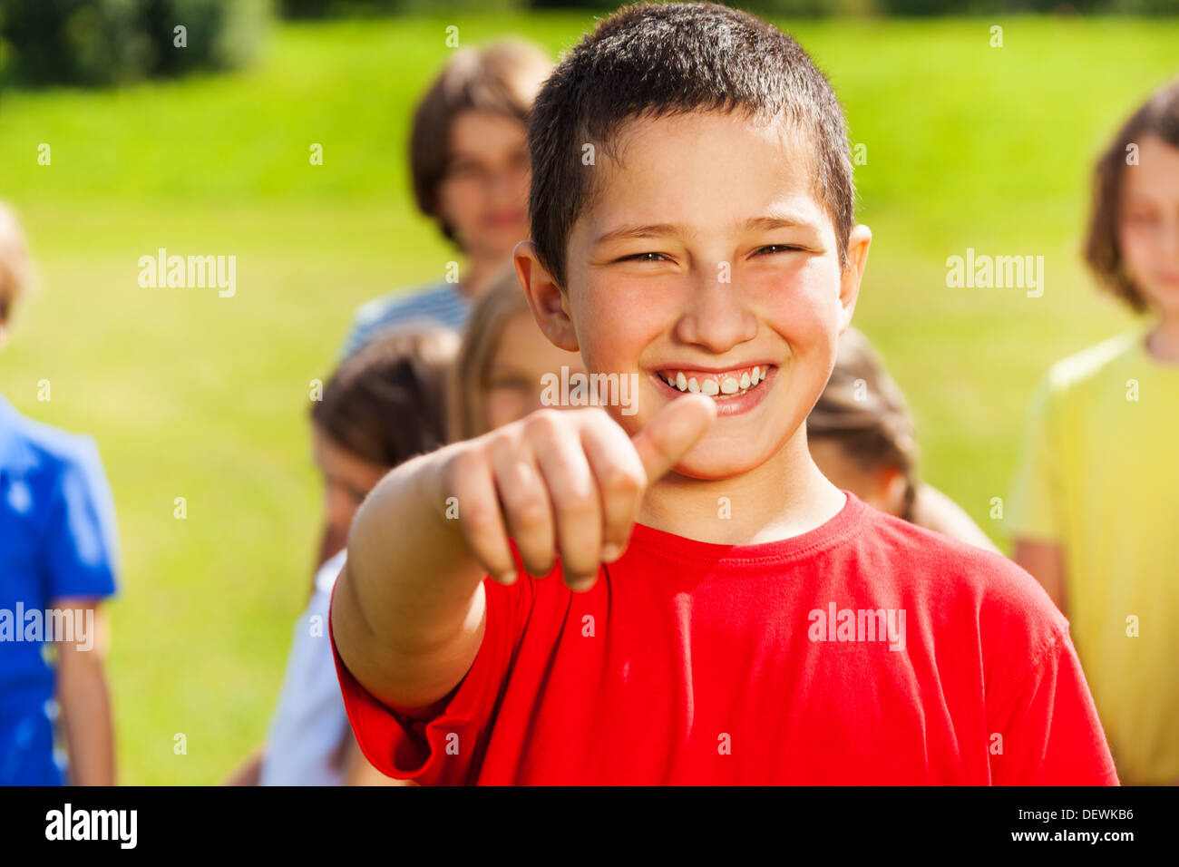 Close portrait of happy Asian boy showing thumb up thumb with group of kids on background Stock Photo