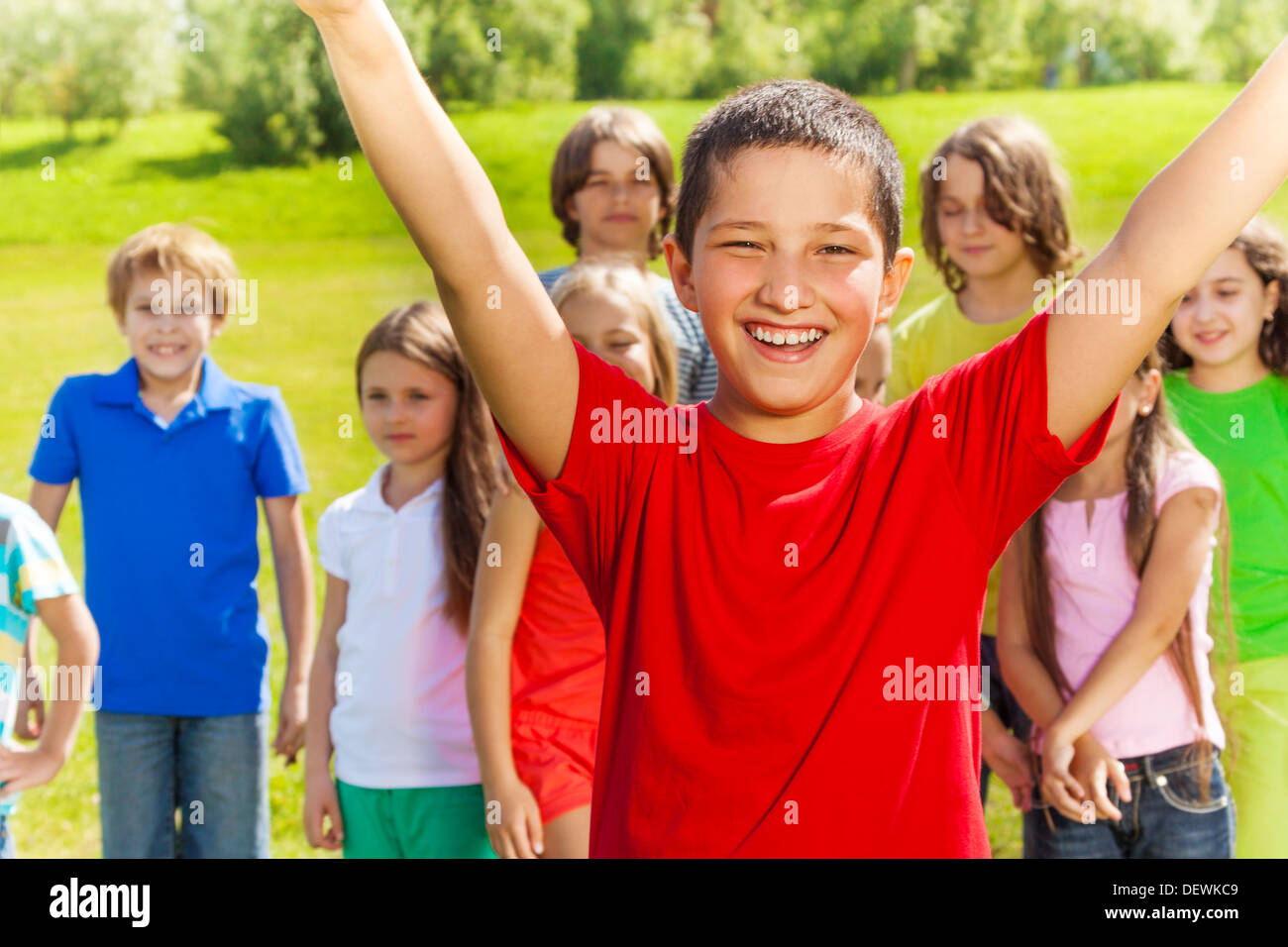 Close portrait of happy Asian boy with lifted hands and very happy expression. His friends and team standing on the background. Stock Photo