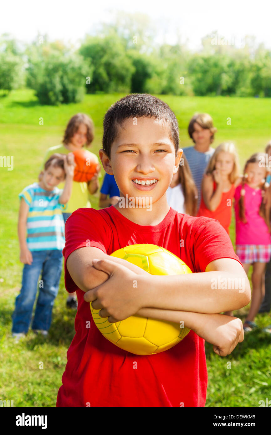 Nice happy smiling Asian boy with volleyball ball standing in the park with his team on background Stock Photo