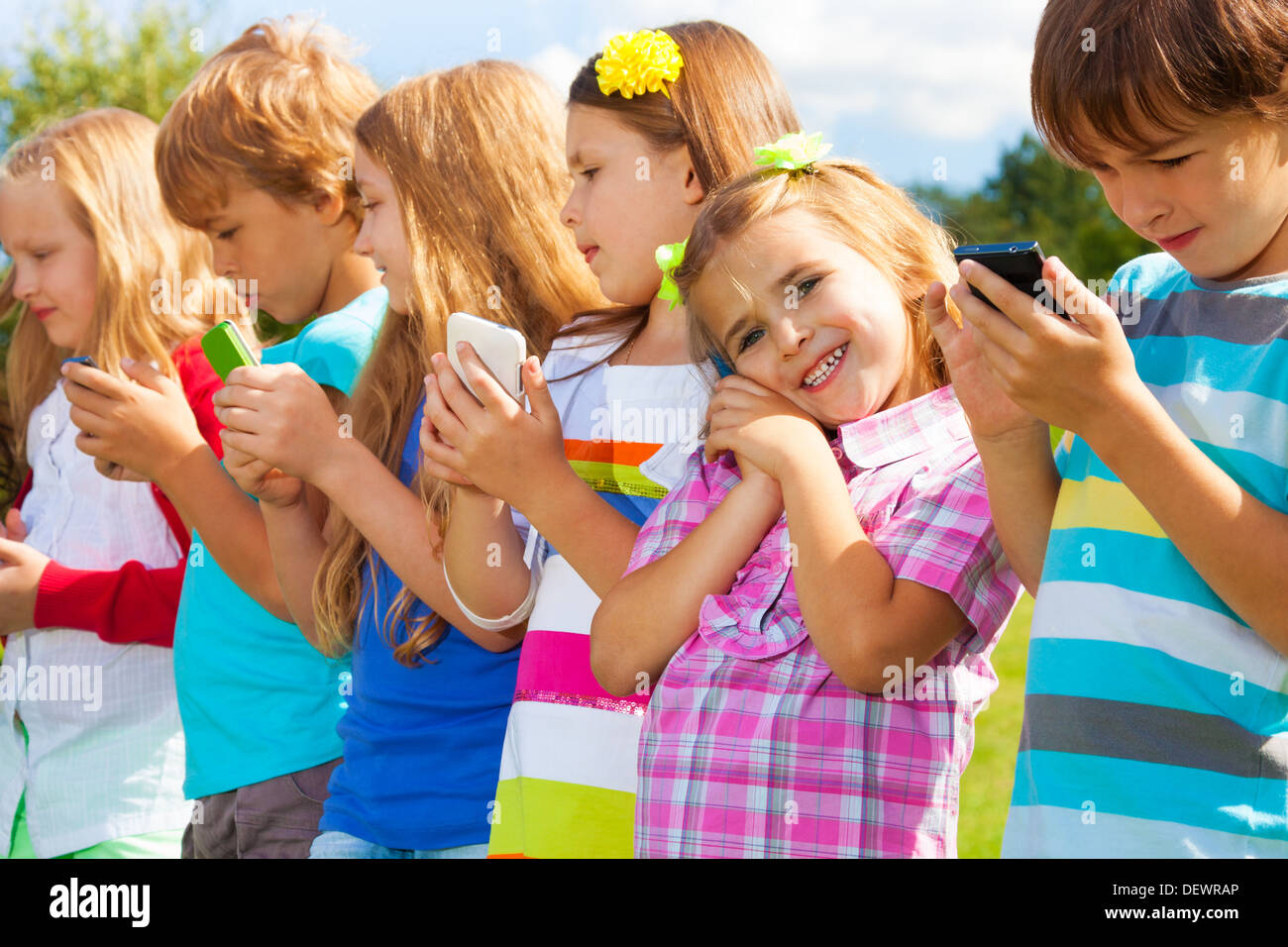 Beautiful group of many kids standing with cell phones talking texting and playing, all outside Stock Photo