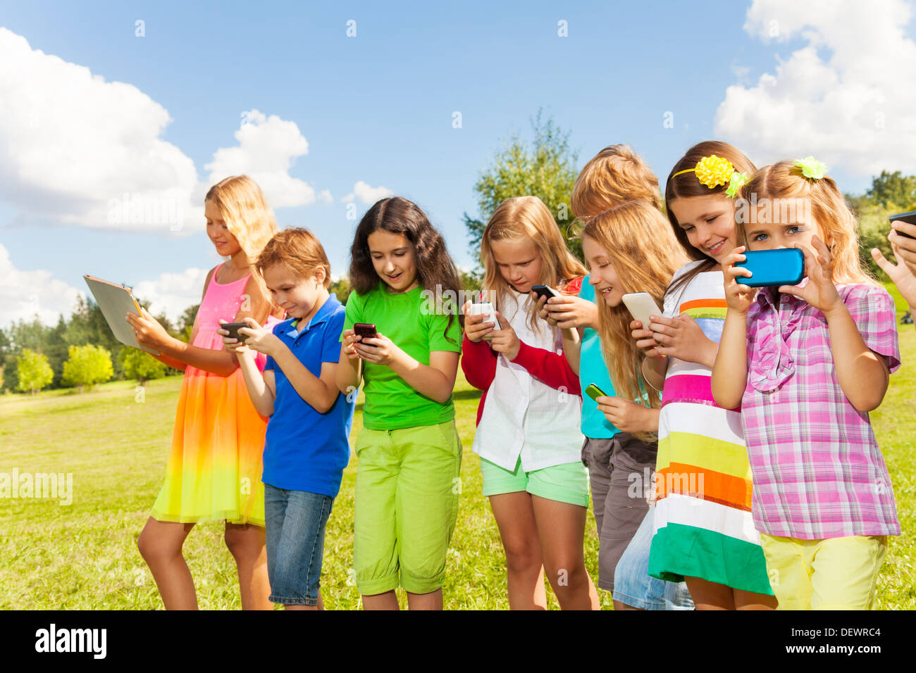 Large group of busy kids, boys and girls looking at their phones texting sms and playing staying outside Stock Photo