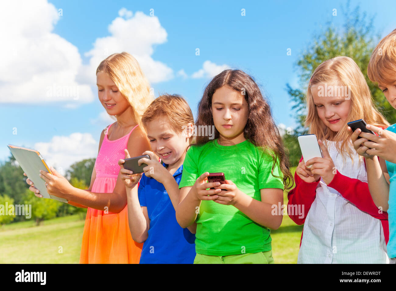 Five happy kids stnading with phones and digital devices Stock Photo