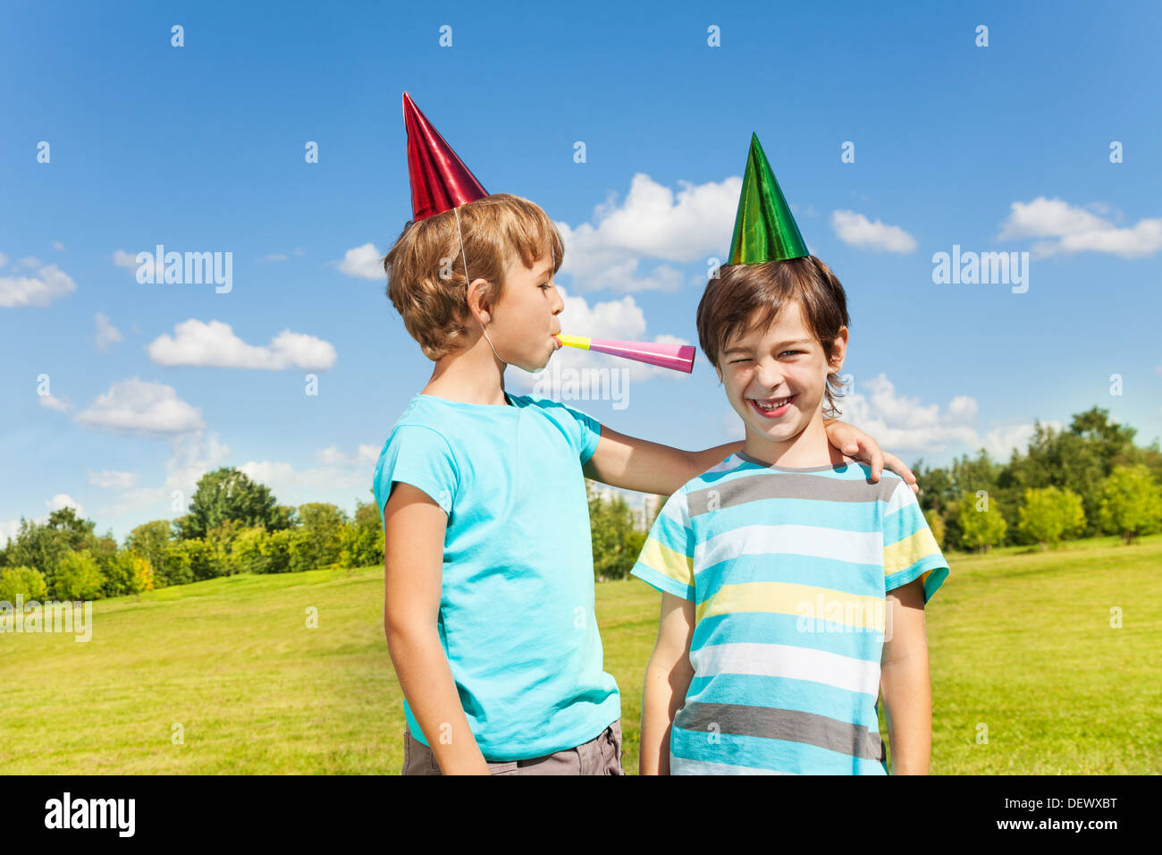 Two boys on birthday party having fun with blowing into noisemaker loudly standing together in the park Stock Photo