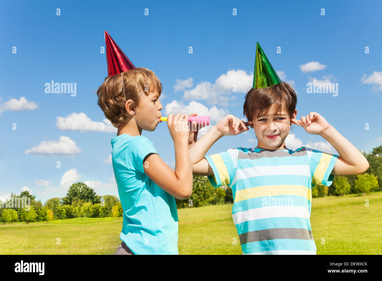 Two boys one with finger in his ears and the other blow loud in the years with nosemaker Stock Photo