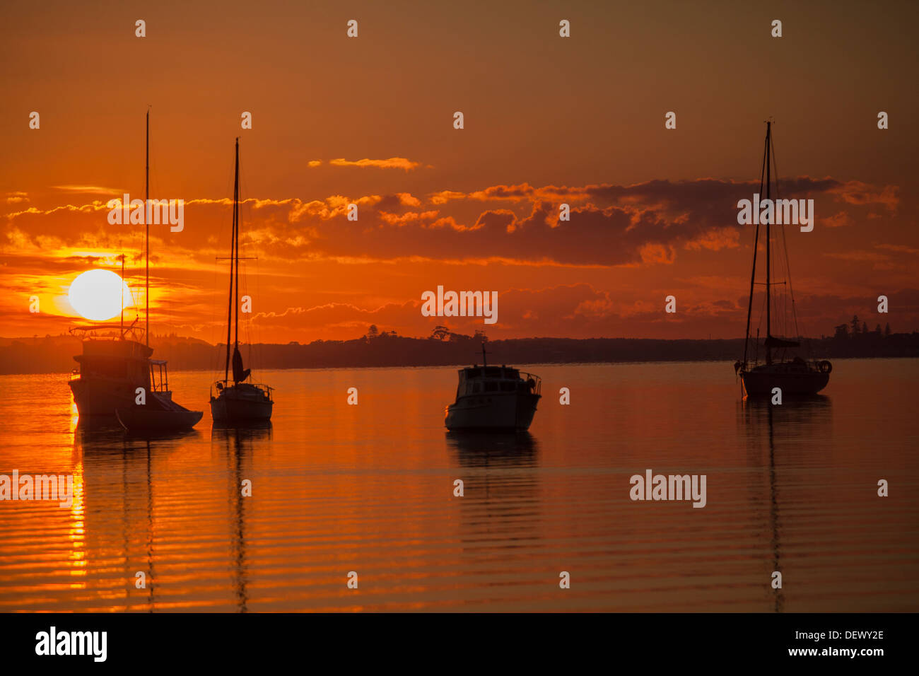 Orange Sunrise with silhouetted boats on Lake Macquarie NSW Australia Stock Photo