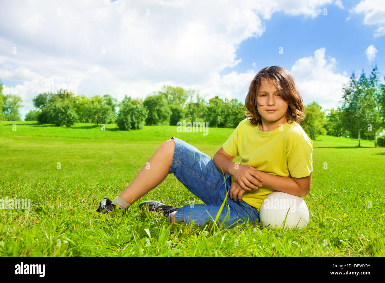 Portrait of 12 years old boy lay in the grass with basketball ball on the field on bright sunny day Stock Photo