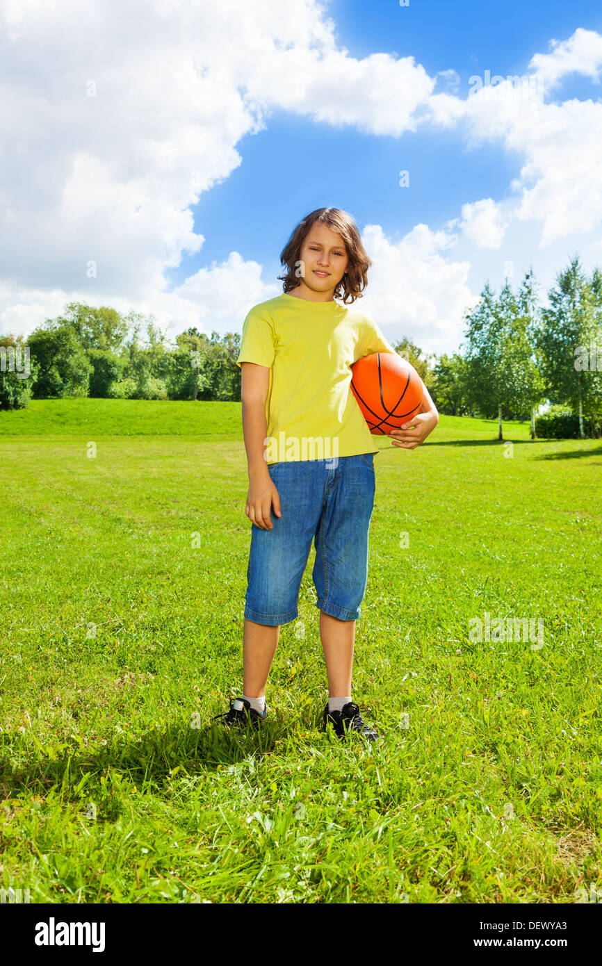 Portrait of 12 years old boy hold basketball ball on the field on bright sunny day Stock Photo