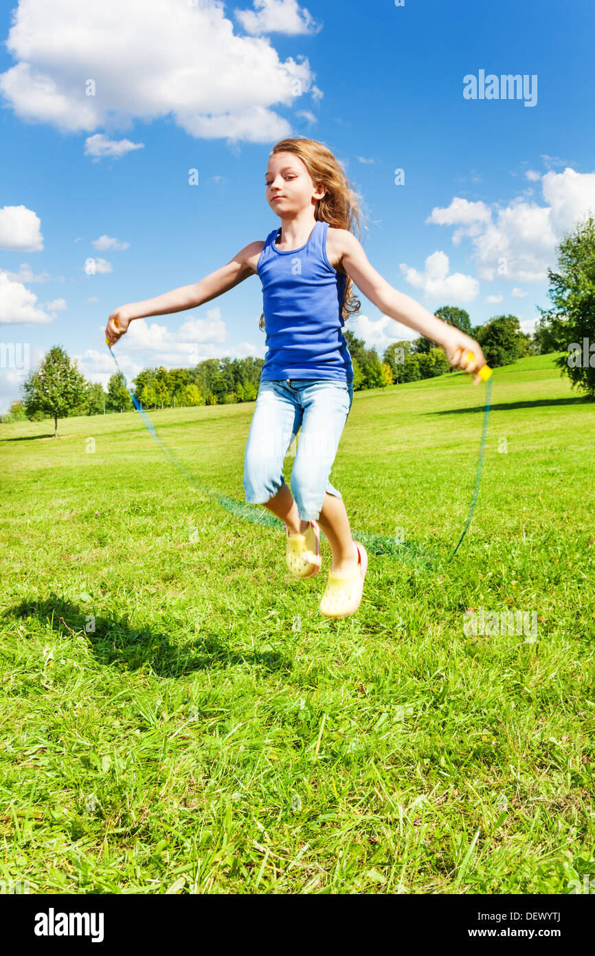 Beautiful girl with skipping rope jumping in the park on green grass field on sunny summer day Stock Photo