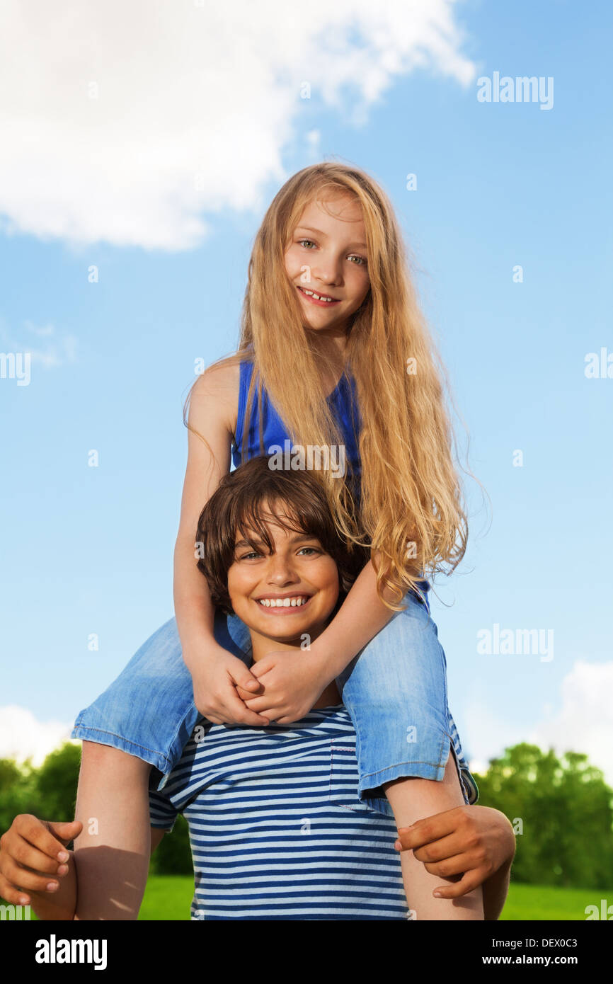 Two kids, boy carry girl on his back, both happy and smiling, in the
