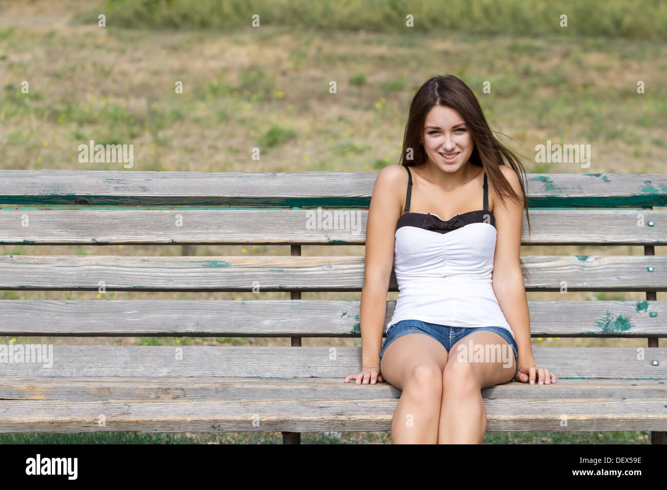 Happy young girl sitting on a bench in a summer day. Shot with lots of ...