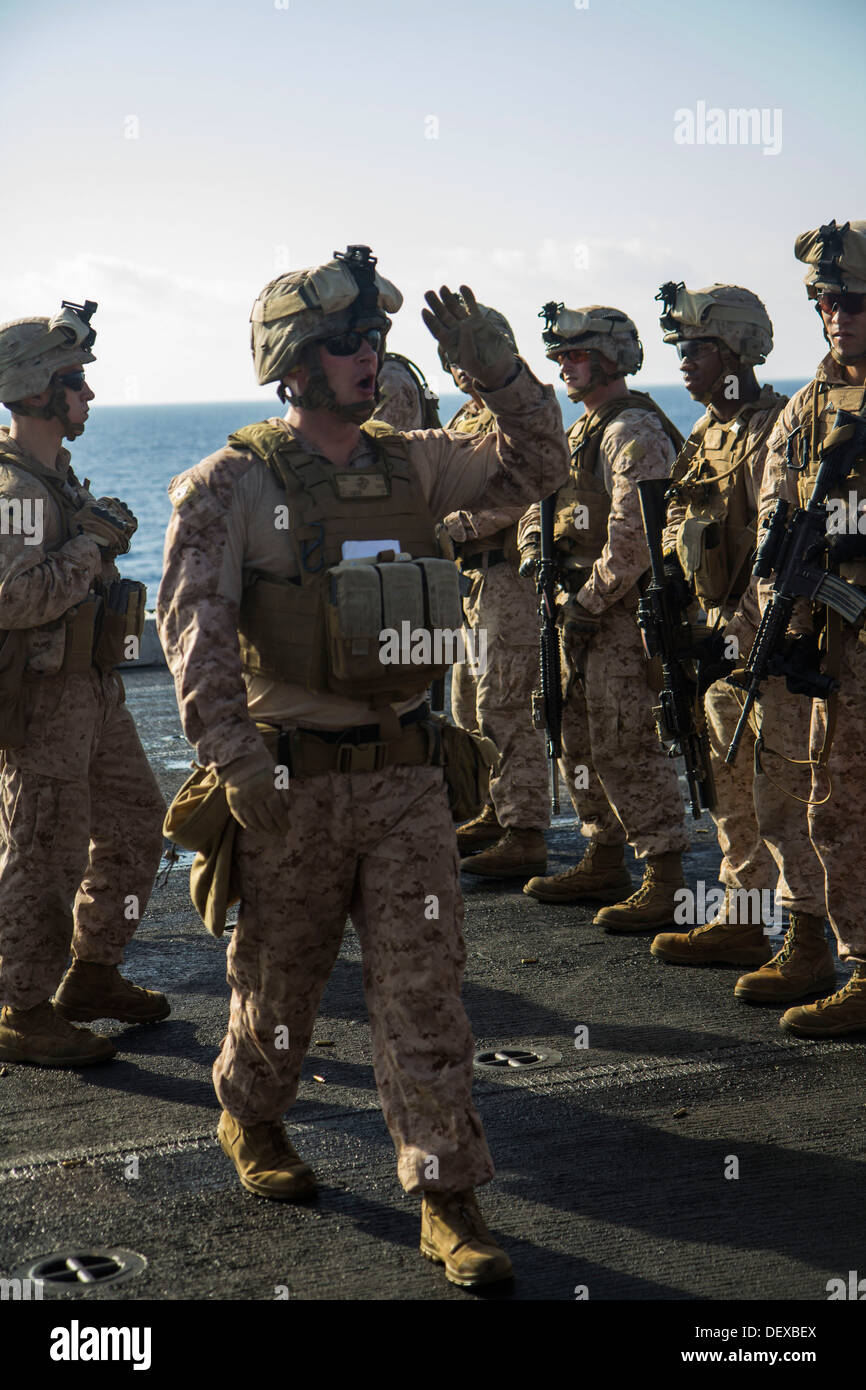 U.S. Marines assigned to Company L, Battalion landing Team 3/2, 26th Marine Expeditionary Unit (MEU), are briefed on target iterations during a live fire exercise on the flight deck of the USS San Antonio (LPD 17), at sea, Sept. 12, 2013. The 26th MEU is Stock Photo