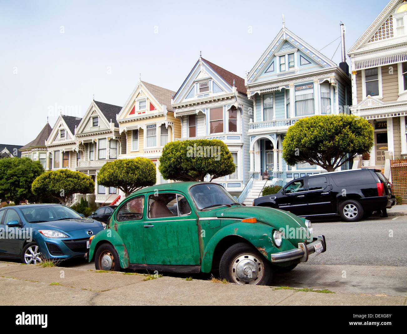 A green Volkswagen Beetle parked in front of the 'Painted Ladies' row of Victorian Houses on Steiner Street in San Francisco. Stock Photo