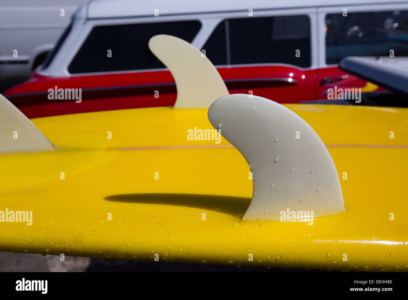 Yellow surfboard keel fins detail eith red retro car in background in
