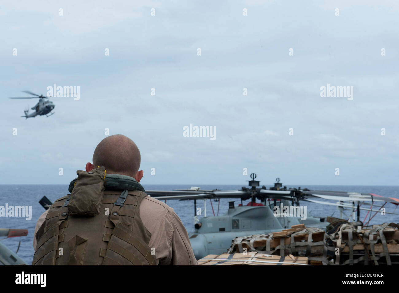 A Marine assigned to the 31st Marine Expeditionary Unit watches a UH-1Y Huey approach forward-deployed amphibious transport dock ship USS Denver (LPD 9). Denver is on patrol with the Bonhomme Richard Amphibious Ready Group and, with the embarked 31st MEU, Stock Photo