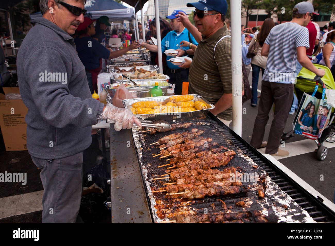 Man grilling chicken skewers on barbecue grill at outdoor festival - USA Stock Photo