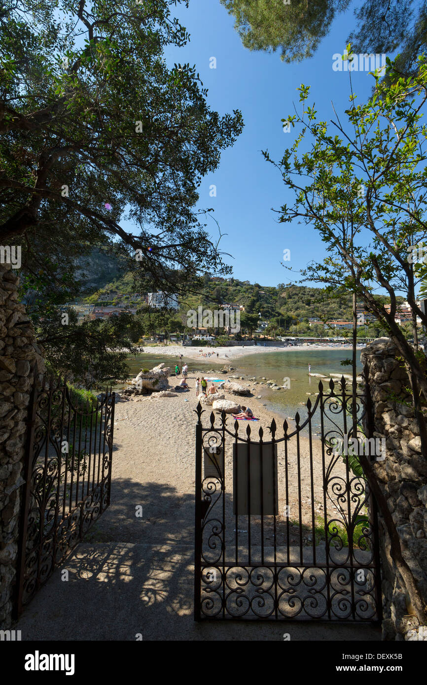 View through a wrought-iron gate at the Isola Bella at Taormina towards the causeway to the mainland and the beach Stock Photo