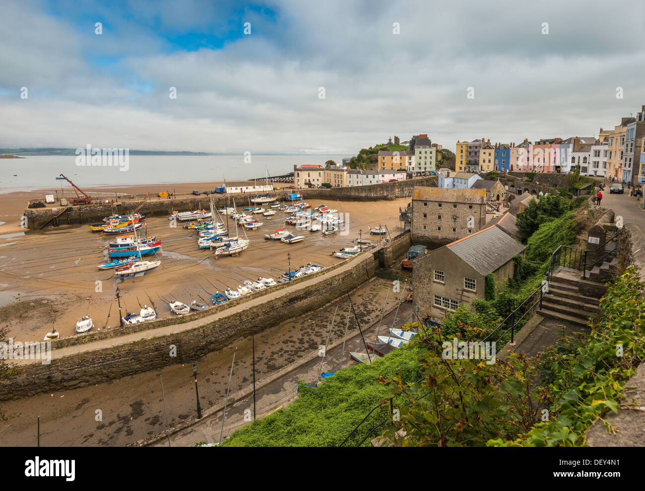 TENBY HARBOUR AT LOW TIDE WITH MOORED BOATS AND CASTLE HILL. TERRACED REGENCY HOUSES IN PASTEL COLOURS. Stock Photo