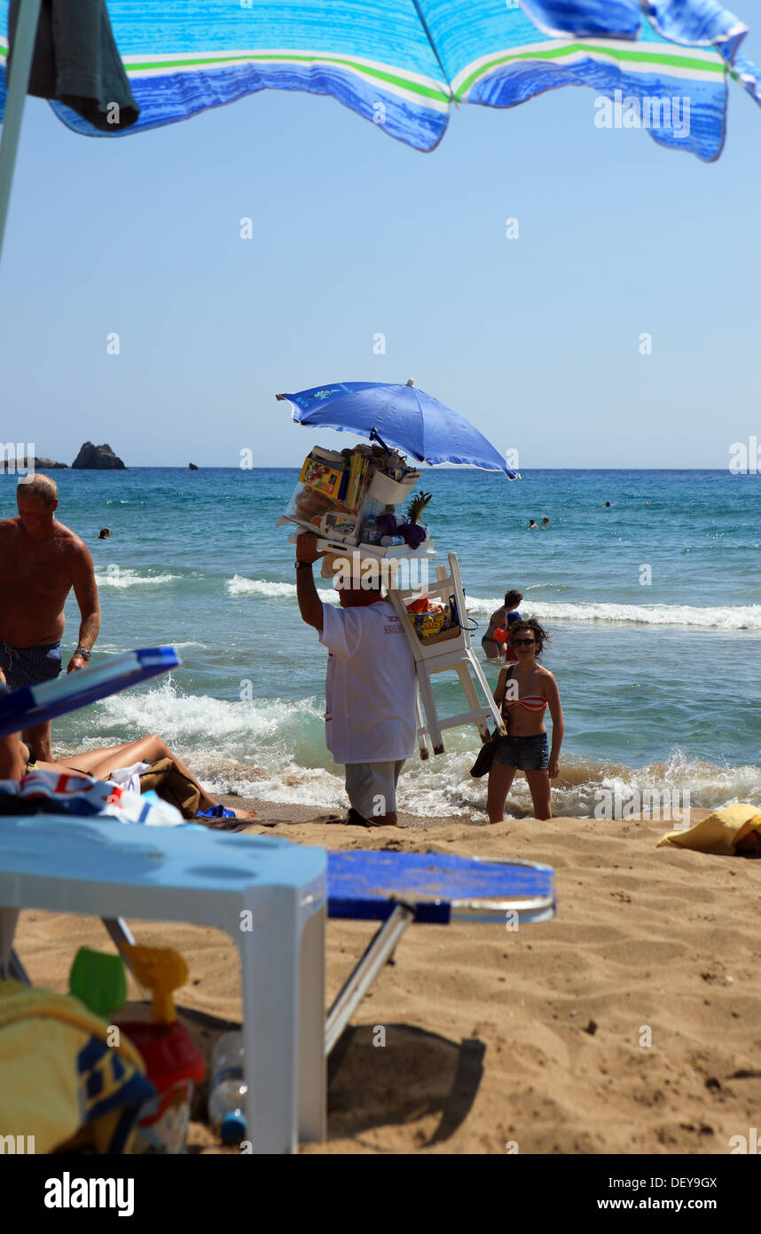 Beach seller carrying a stool and with his produce on a tray on his head in Corfu, Greece Stock Photo