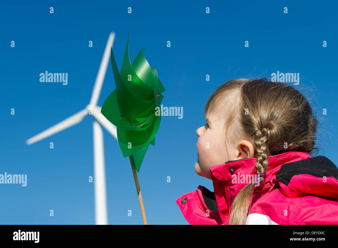 Girl holding a small pinwheel in front of a large wind turbine Stock Photo