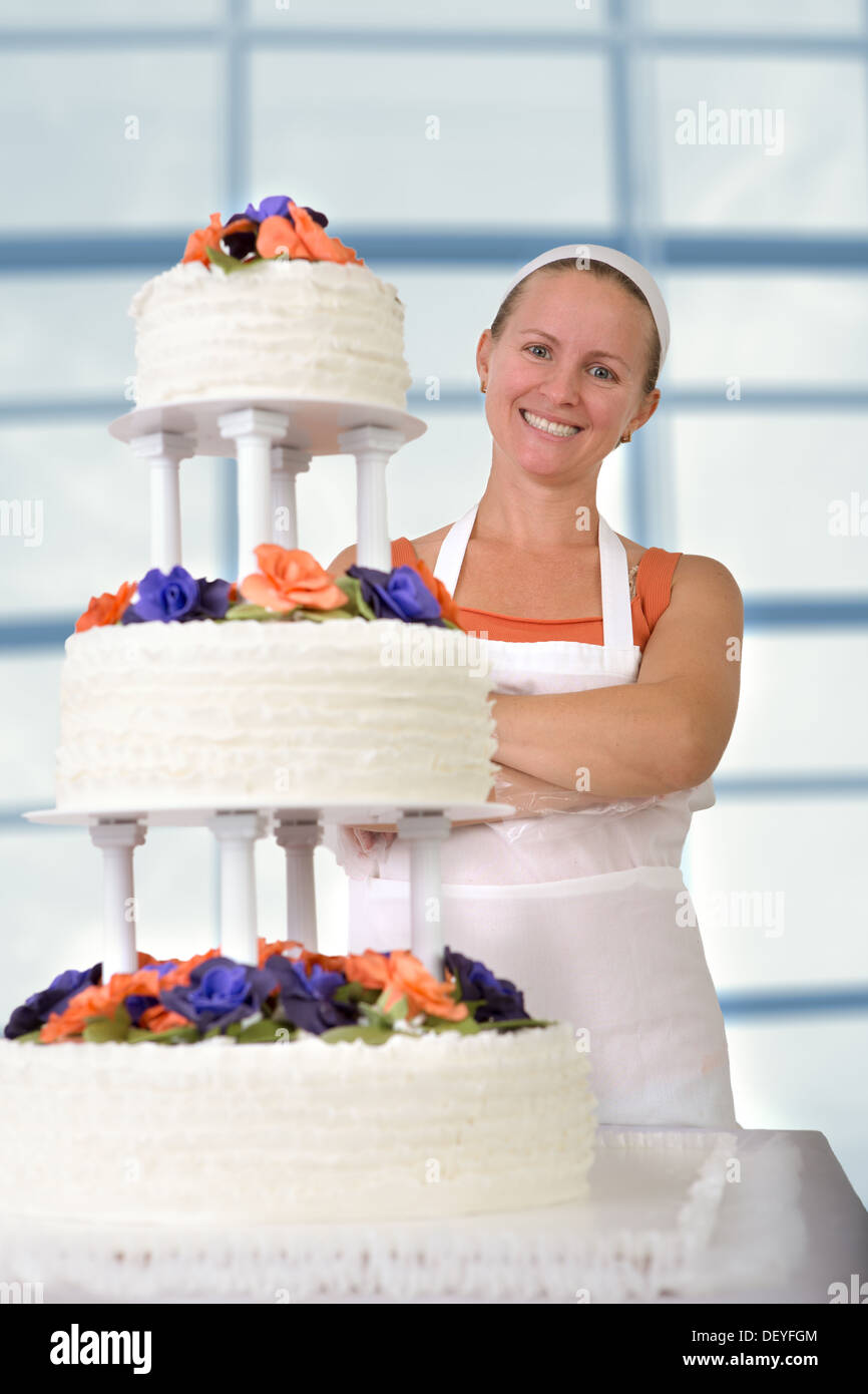 Happy baker lady happily smiling large infront of her cake with her apron and white bandanna, cake has fondant ruffles on the si Stock Photo