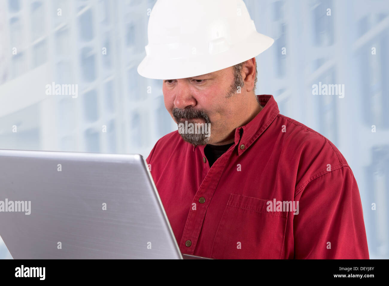 Hardhat worker working on the tough issues with his laptop, he has a serious thoughtful look that he values his job Stock Photo