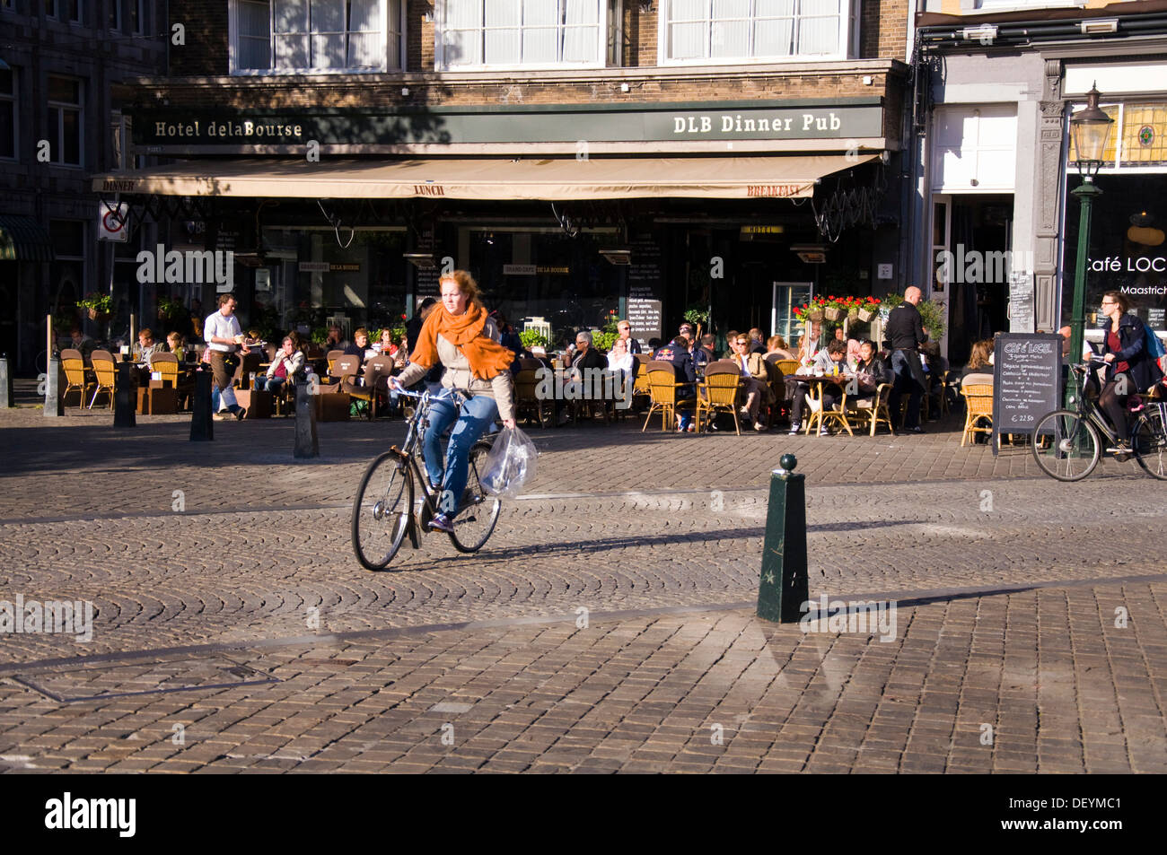 Woman cycles past Hotel de la Bourse restaurant cafe bar pub on Markt Maastricht Netherlands Stock Photo