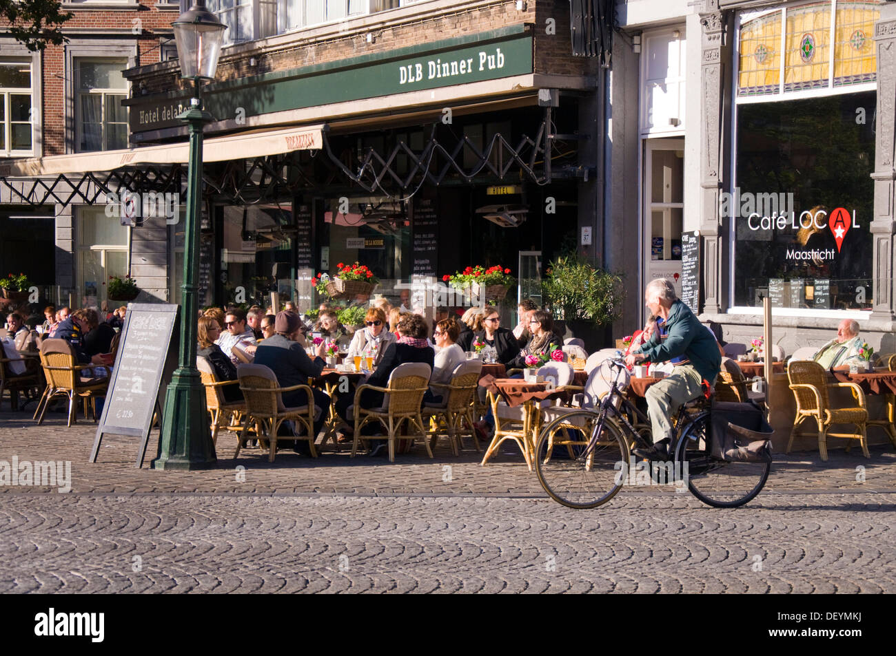 Man cycles past Hotel de la Bourse restaurant cafe bar pub on Markt Maastricht Netherlands Stock Photo