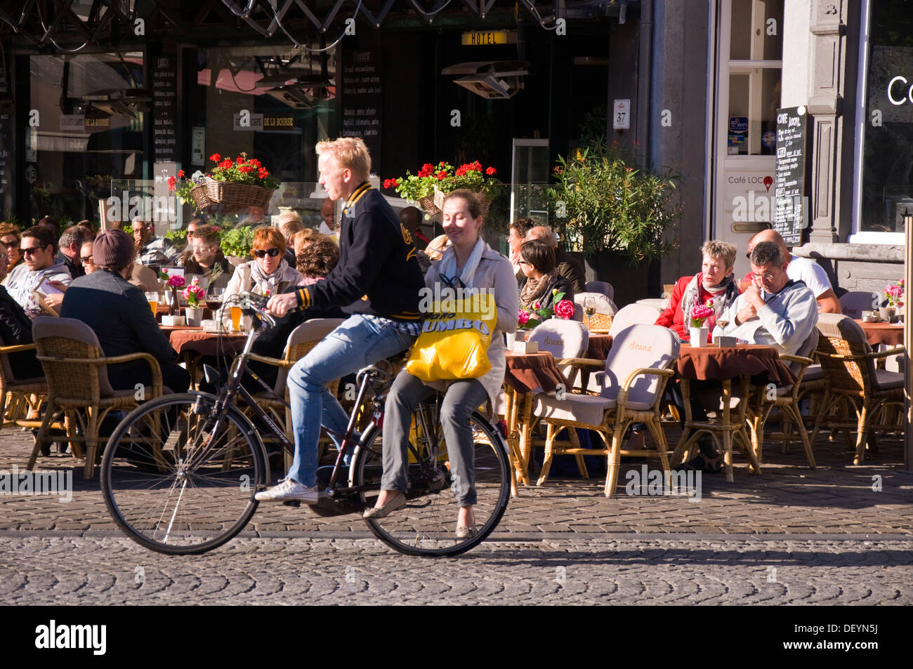 Customers sit outside Hotel de la Bourse restaurant cafe bar pub on Markt Maastricht Netherlands as a cyclist passes by Stock Photo