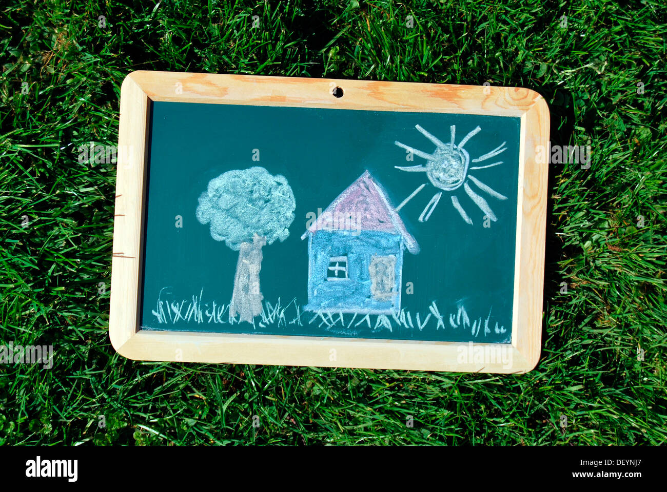 Chalk drawing, house with garden and sun drawn on a school chalkboard lying on a meadow Stock Photo