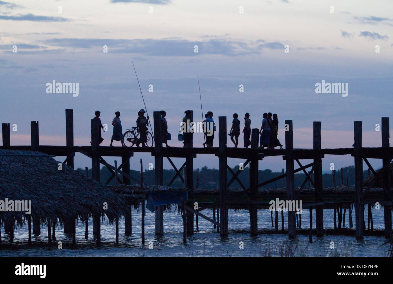 People walk across U Bein's Bridge at sunset on Taungthaman Lake ...