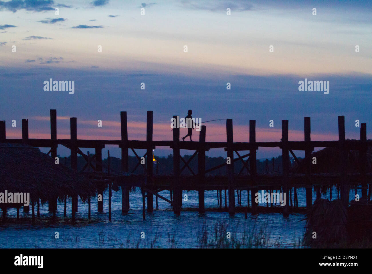 People walk across U Bein's Bridge at sunset on Taungthaman Lake ...