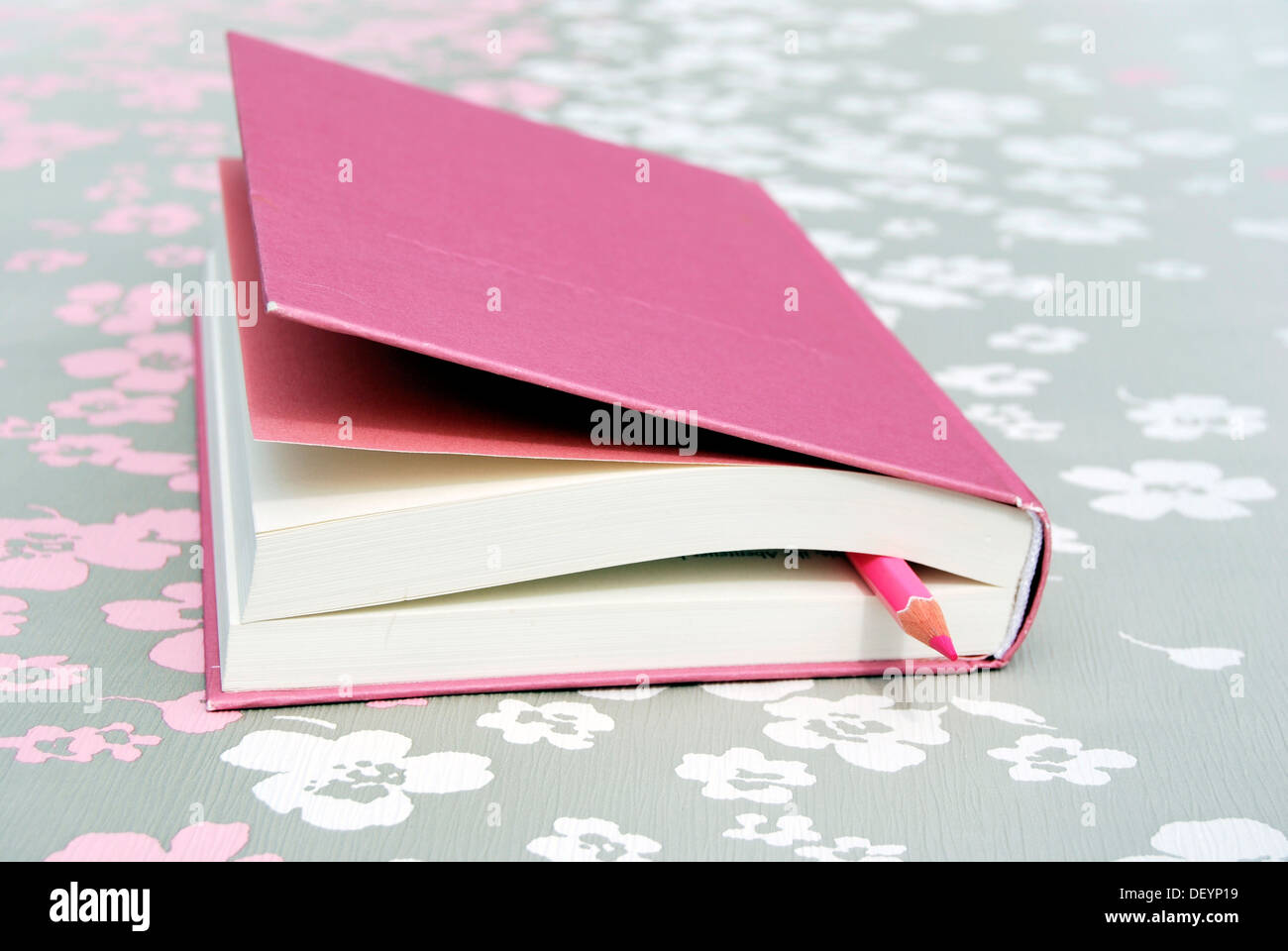 Closed pink book with pen as a bookmark, on floral design Stock Photo