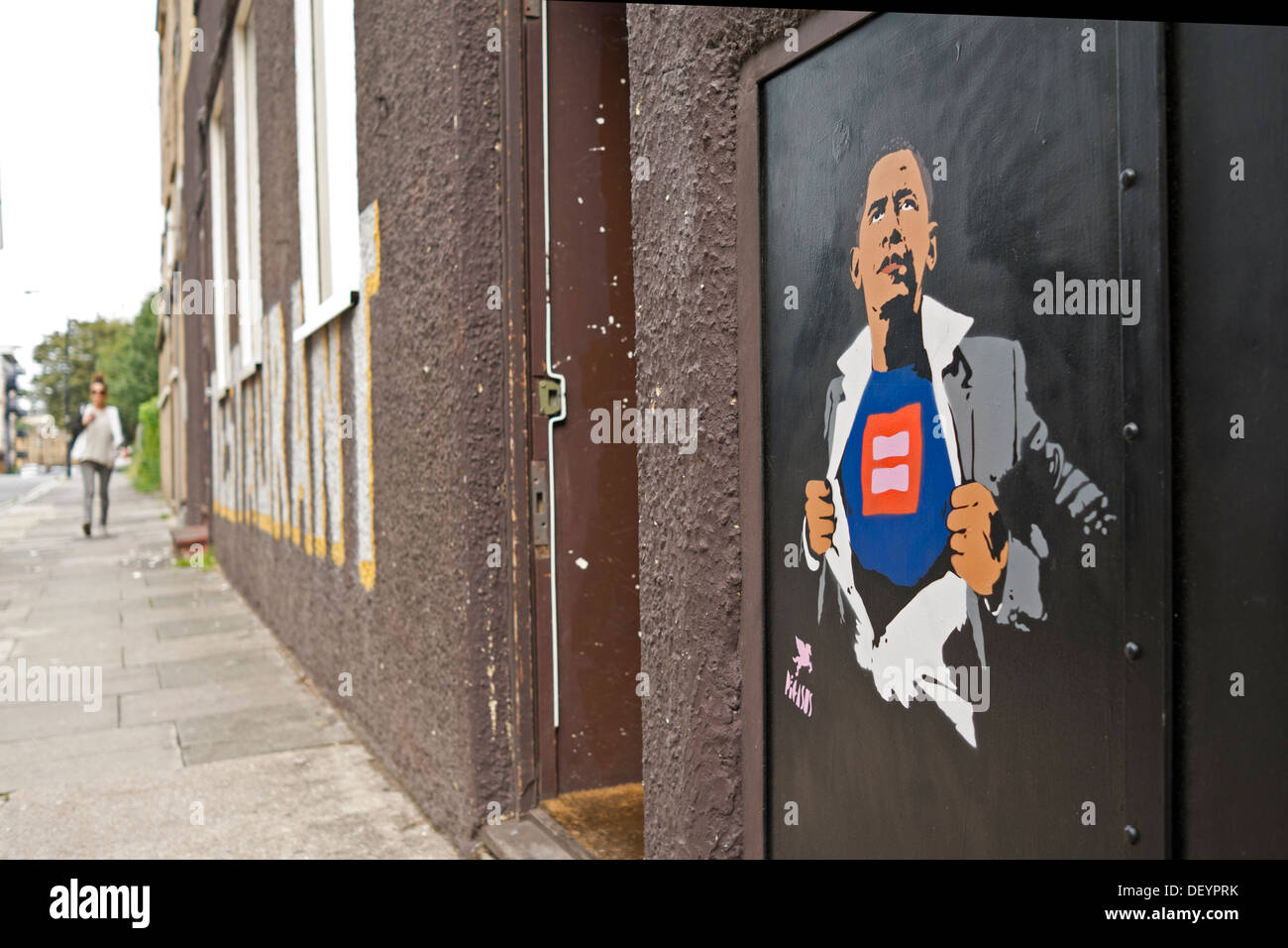 A girl walks up a street in the distance. A stenciled graffiti image of President Barack Obama has been painted on the wall. Stock Photo
