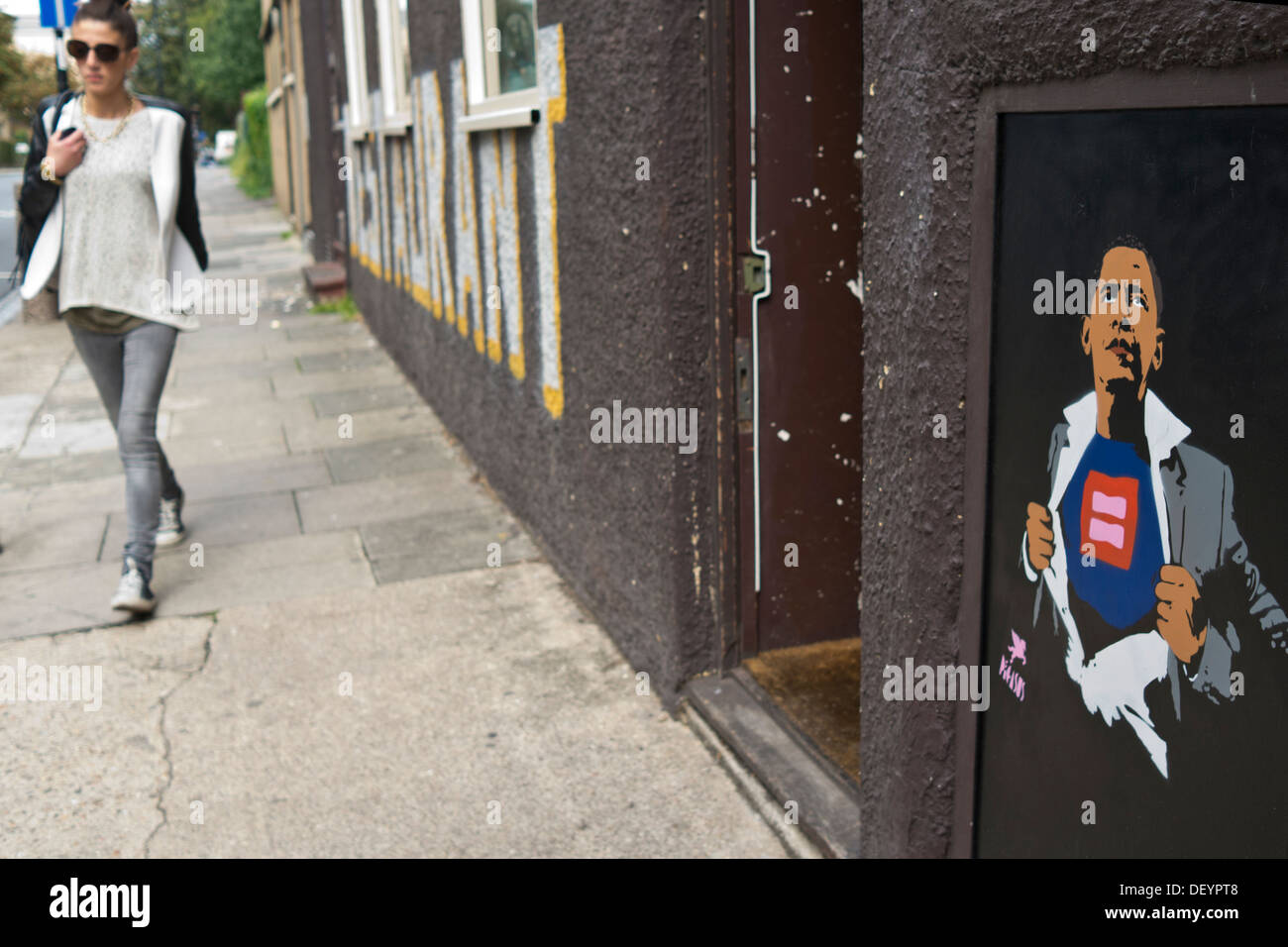 A girl walks along a street, a graffiti image of President Barack Obama has been painted on the wall. Stock Photo