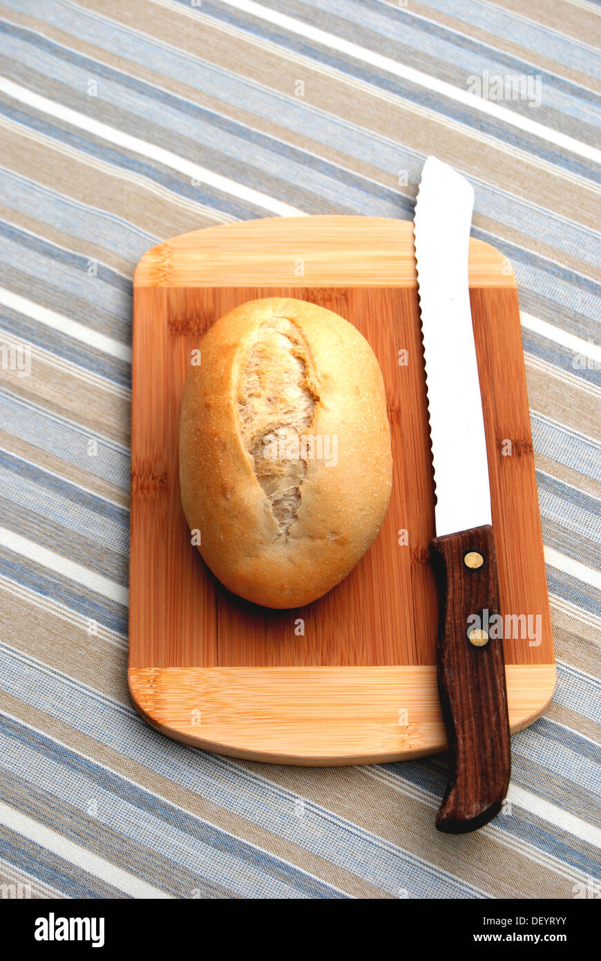 Bread roll on a wooden board, chopping board, bread knife, striped table cloth Stock Photo