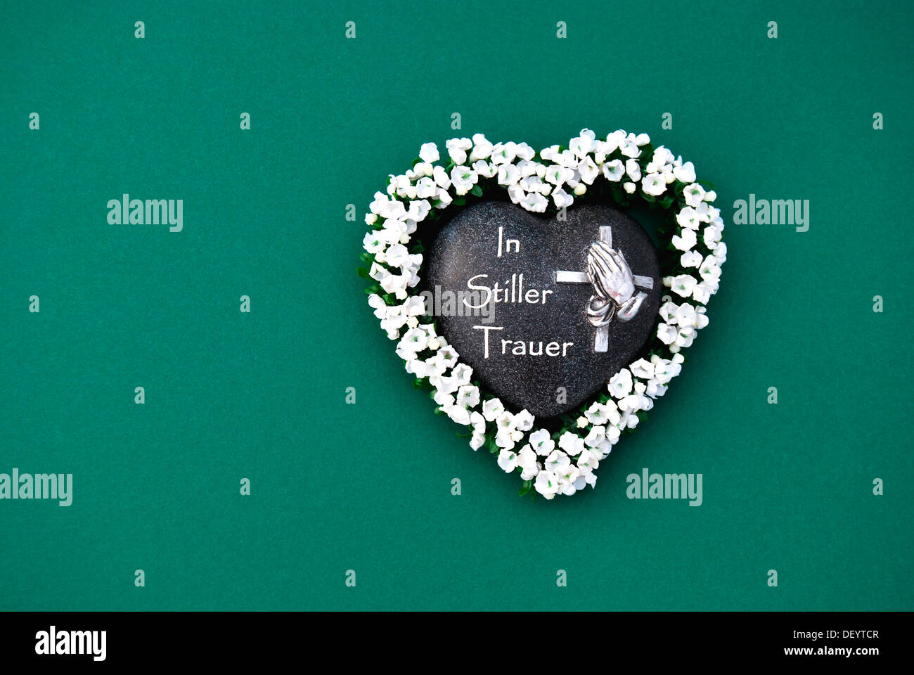 Heart of stone with the inscription 'In Stiller Trauer', German for 'In silent grief', heart-shaped stone framed with flowers Stock Photo