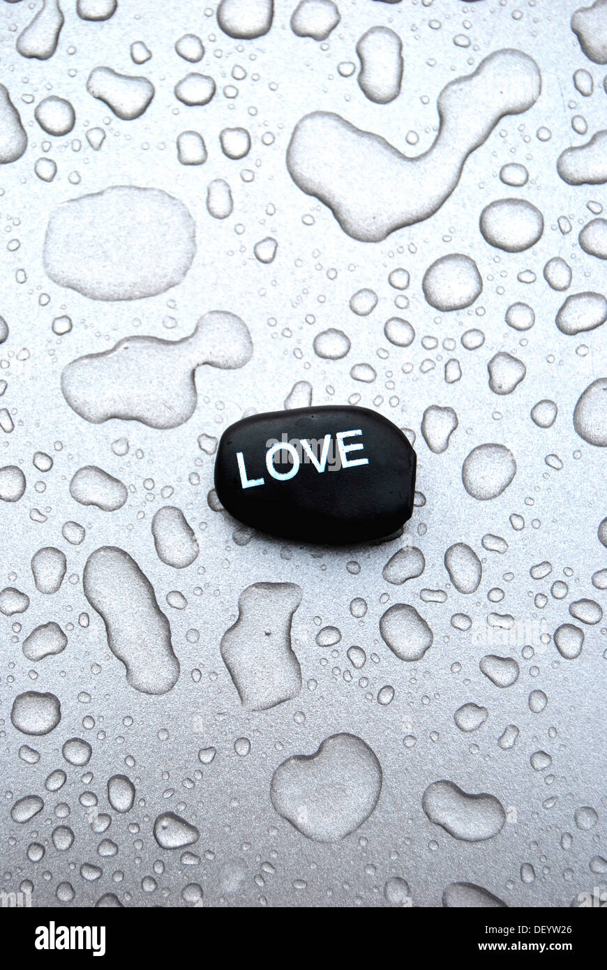 Hot stone massage stone with the inscription Love on a surface with water drops Stock Photo