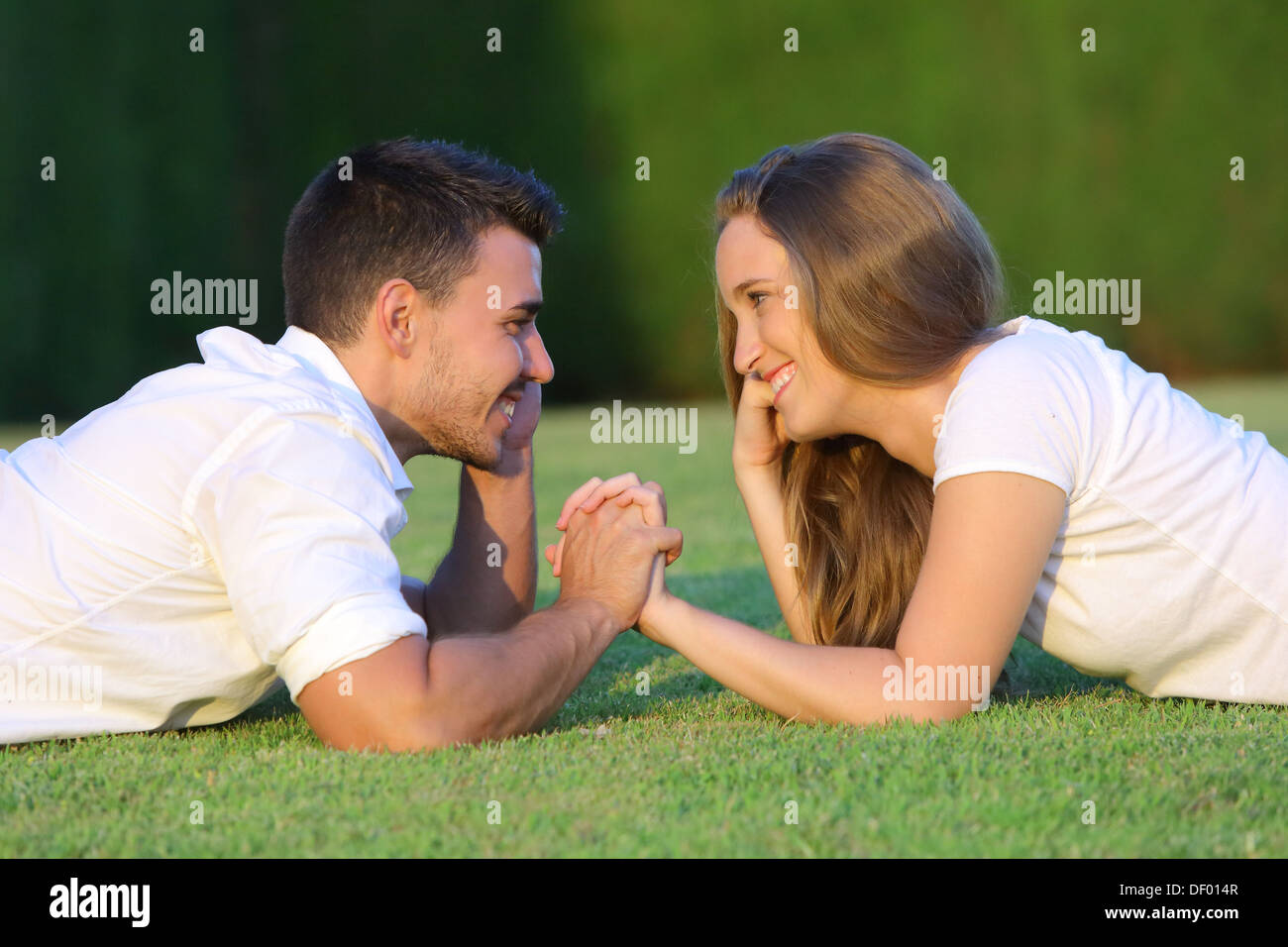 Profile of a couple in love flirting and looking each other lying on the grass with a green background Stock Photo