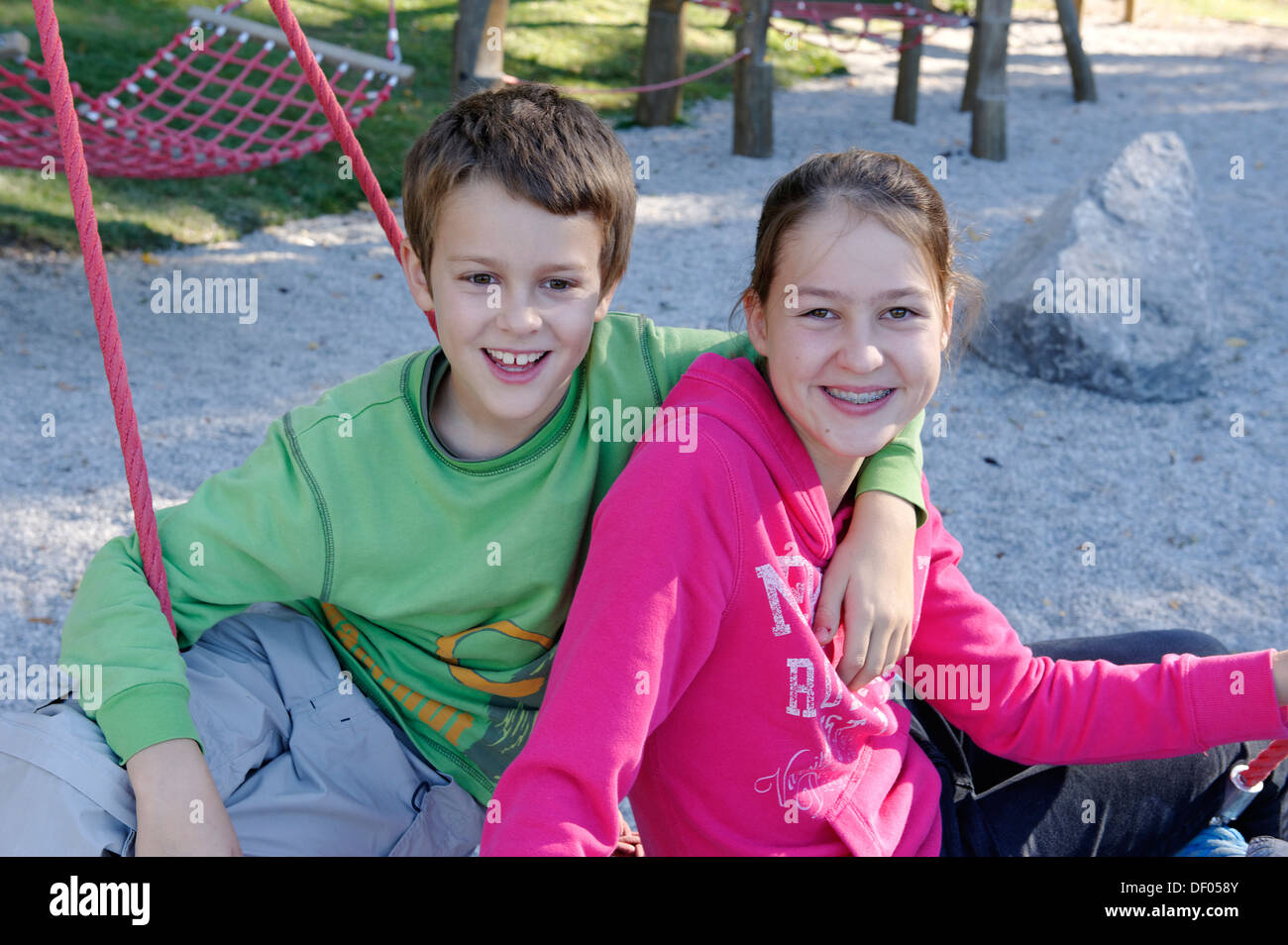 A boy and girl sitting on a playground, Schliersbergalm alp, near lake Schliersee, Upper Bavaria, Bavaria Stock Photo