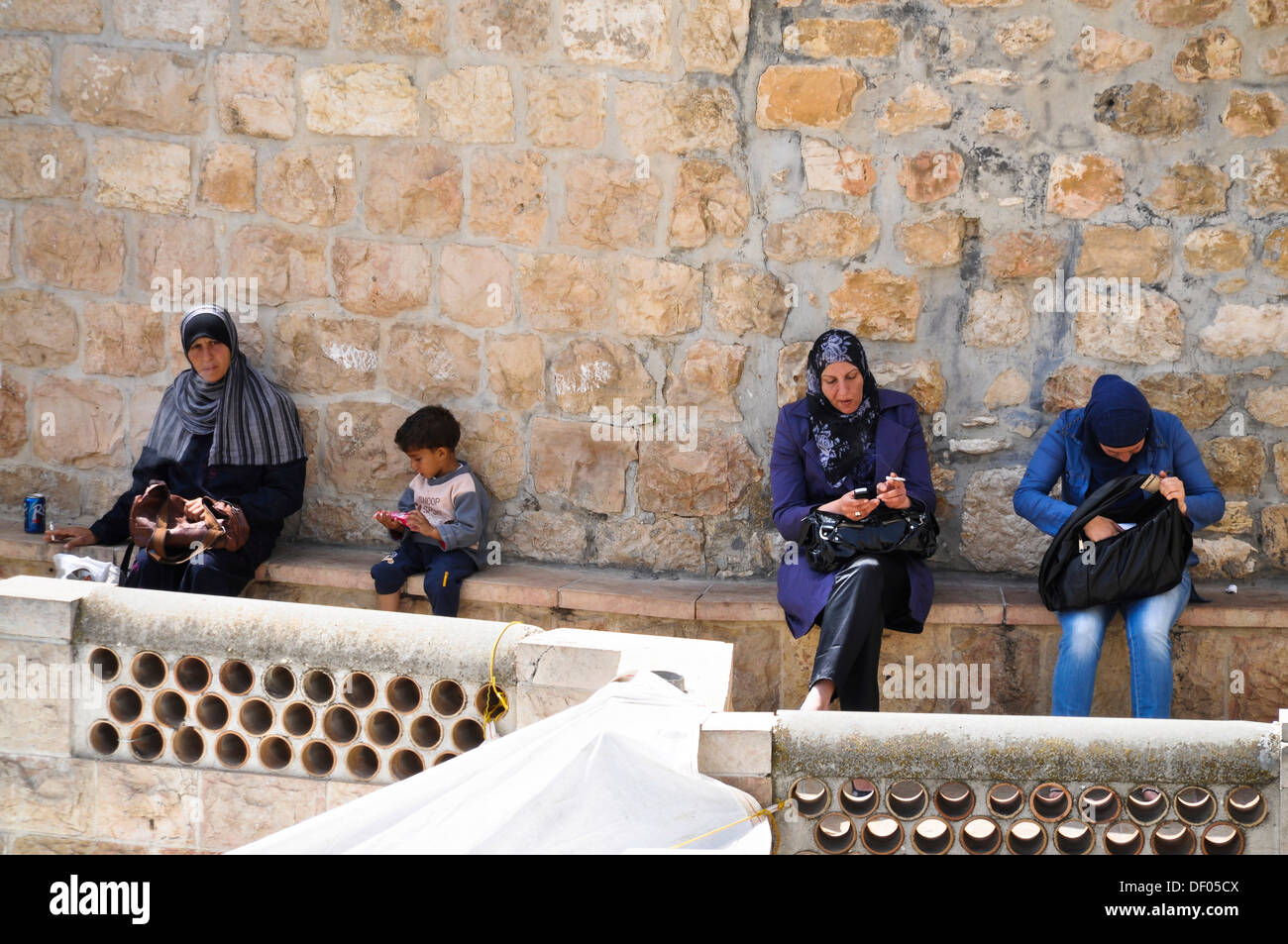 Veiled women smoking cigarettes and cell phones and a boy sitting on the city wall, Jerusalem, Israel, Middle East Stock Photo