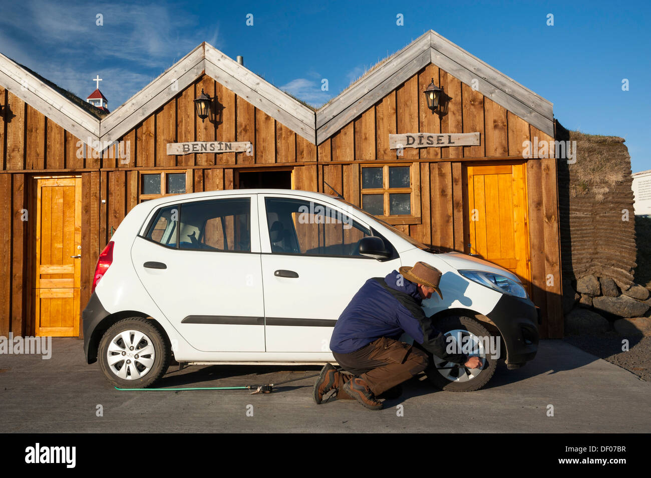 Man kneeling next to a car checking the tyre pressure, petrol station