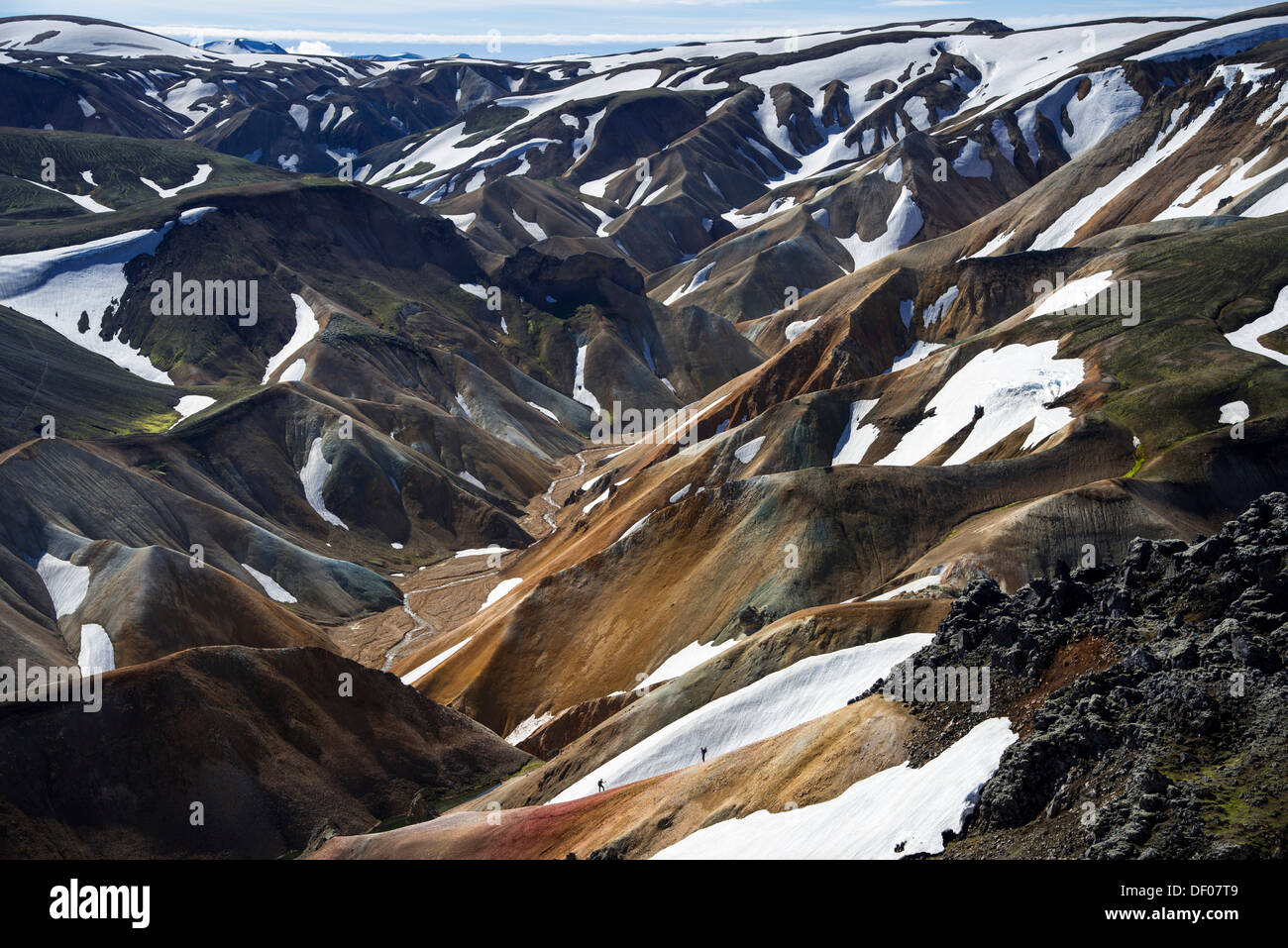Hikers on a trail, view from the Brennisteinsalda volcano to the snow-capped rhyolite mountains, Landmannalaugar Stock Photo