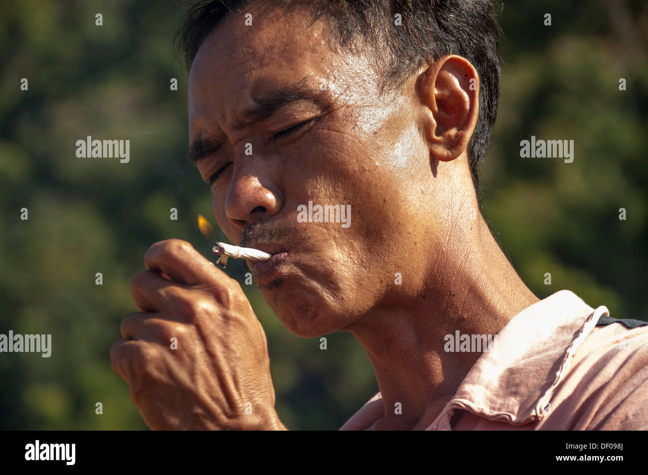 Man from the Shan or Thai Yai ethnic minority is lighting a cigarette, Soppong or Pang Mapha area, Northern Thailand, Thailand Stock Photo