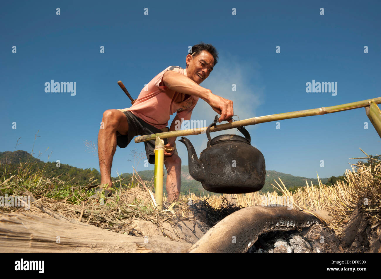 Man from the Shan or Thai Yai ethnic minority, is boiling water in an iron kettle, Soppong or Pang Mapha area, Northern Thailand Stock Photo