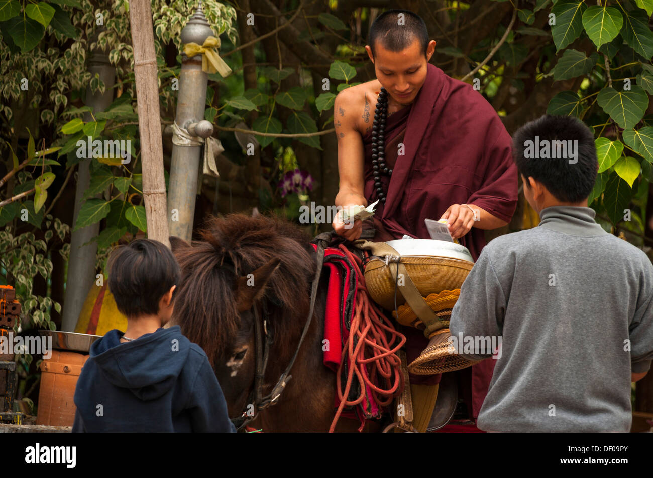 Buddhist monk on horseback with a begging bowl collecting alms in the morning, temple and monastery of Wat Phra Archa Thong or Stock Photo