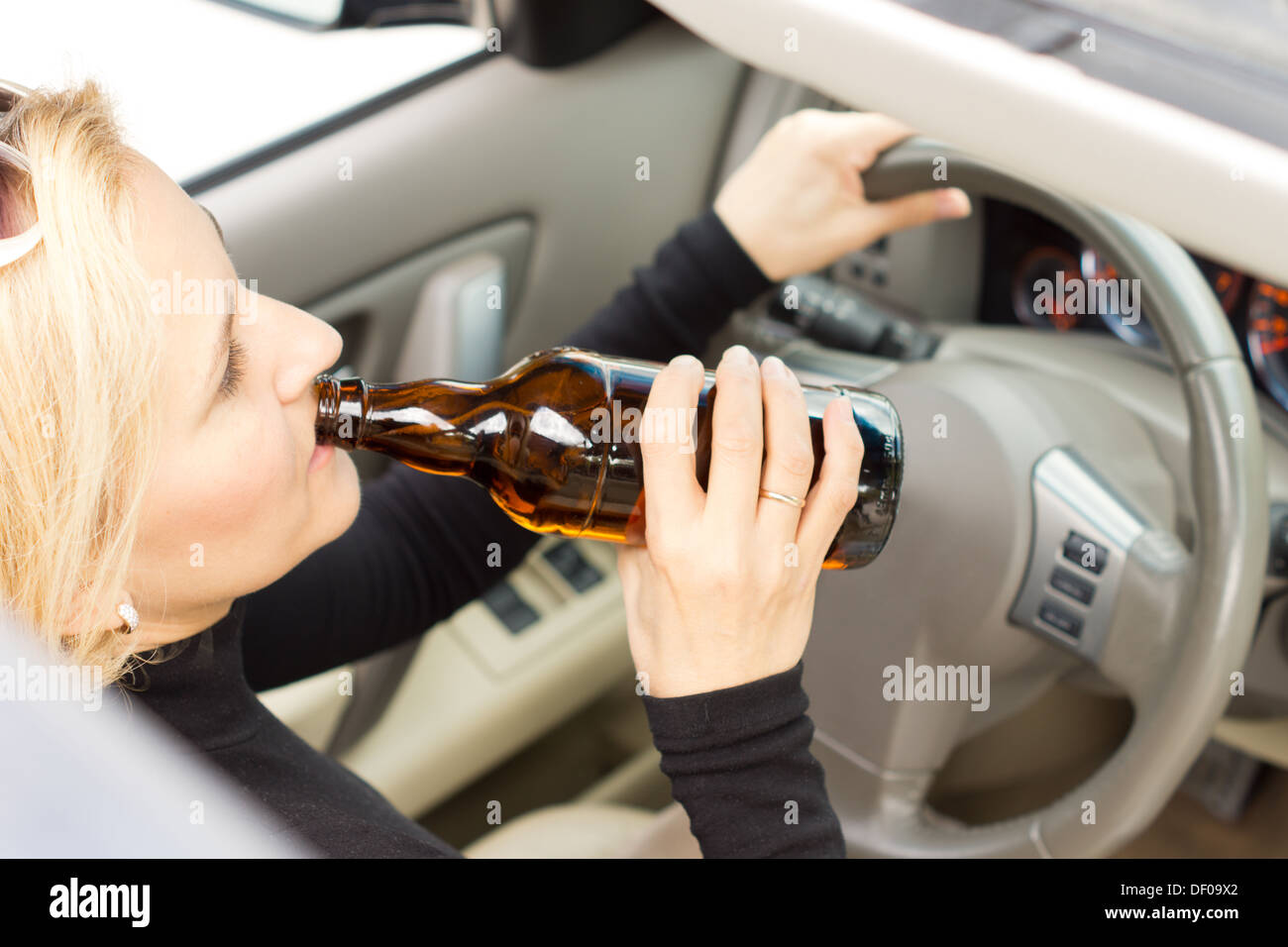 High angle view of a drunk woman driver sitting behind her steering wheel imbibing from a bottle of alcohol as she drives Stock Photo