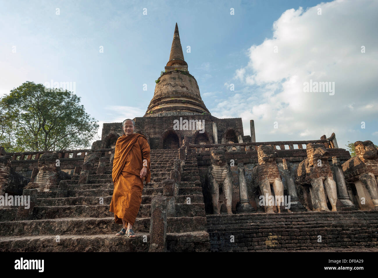 Buddhist monk on the stairs, laterite chedi with destroyed elephant statues, stepped temple of Wat Chang Lom Stock Photo