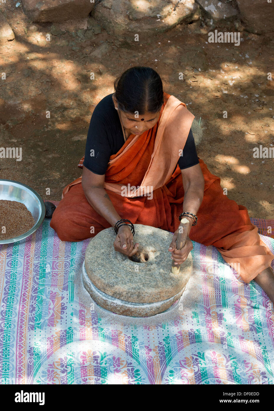 Rural Indian village woman using Quern stones to grind Finger Millet seed / Ragi seeds into Ragi flour. Andhra Pradesh. India Stock Photo